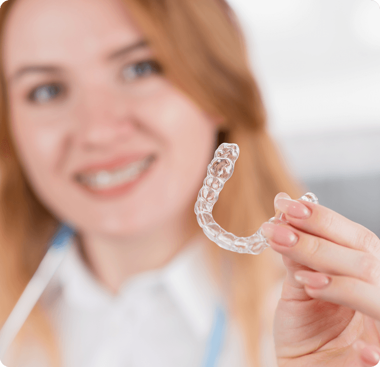 Woman smiling while holding clear aligners