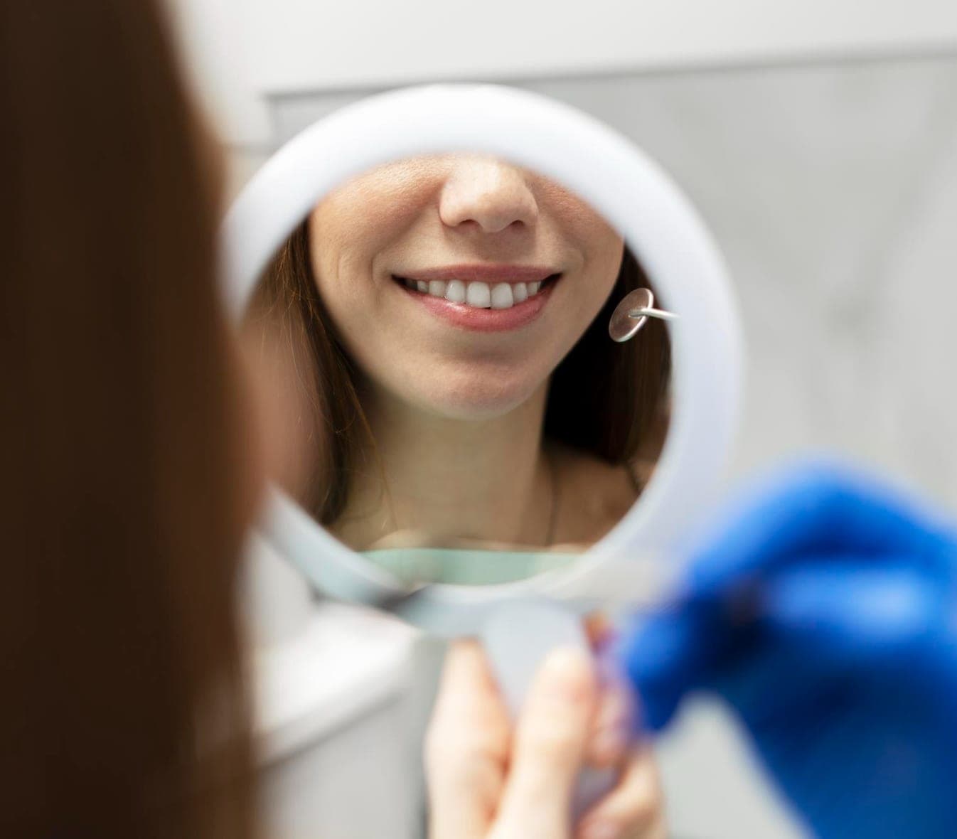 Patient smiling into a hand mirror after a cleaning